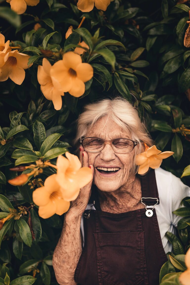 Old woman happily standing in a flower garden